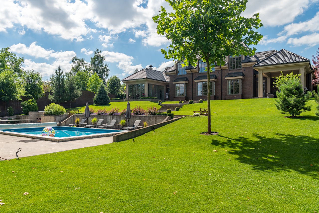 About Spacious elegant mansion with a pristine pool, lush garden, and clear blue sky.